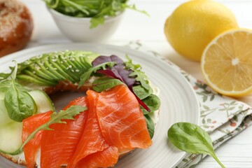 Delicious bagel with salmon, cream cheese, cucumber and avocado on white wooden table, closeup