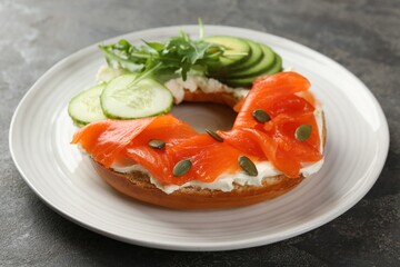 Delicious bagel with salmon, cream cheese, cucumber, avocado and pumpkin seeds on grey table, closeup