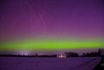 A snowy winter night with the Northern Lights glowing over a field, a shooting star in the sky, and...