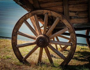 Obraz premium An old wooden wagon wheel rests on a grassy field, illuminated by sunlight.
