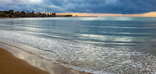 Panorama of the beach sea with the peninsula of the old city in calm with reflection of the cloudy sky after sunset. Low season. Mediterranean, Side, Antalya province, Turkey