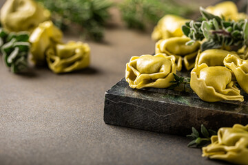 Raw tortellini filled with ricotta and spinach, beautifully arranged on a dark green textured surface and garnished with fresh herbs for a charming rustic look. Background with space for text
