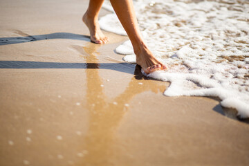 Walking barefoot on wet sandy beach with sea foam