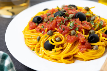 Italian Pasta puttanesca with tomato sauce, capers, and black olives on black slate background. Close up