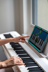 Fototapeta premium Young woman playing a keyboard while pointing at a learning app on a tablet. Technology enhances self-education in music, making learning more intuitive and engaging