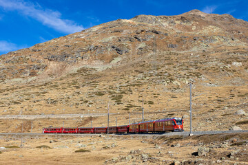Samedan, Switzerland - 31 October 2024: View of scenic Bernina Express train traveling through majestic mountains and beautiful landscape, Samedan, Switzerland.