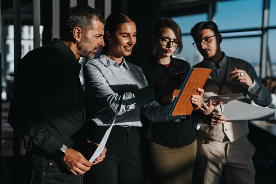 A diverse group of business people engage in a collaborative discussion. The team is reviewing documents and using a tablet, highlighting teamwork and communication in a modern office environment.