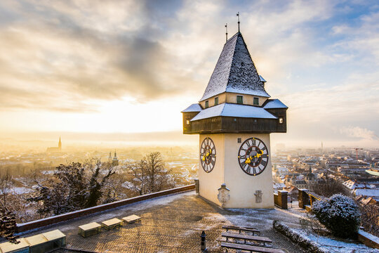 View of snow-covered cityscape with uhrturm clocktower at sunrise, Graz, Austria.