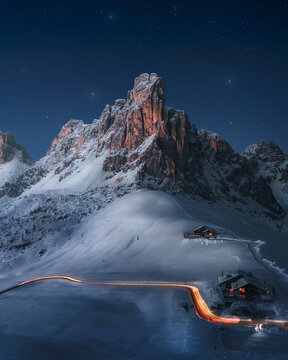 View of tranquil snowcapped mountains under a starry sky with a cozy cabin and light trails, Colle Santa Lucia, Italy.