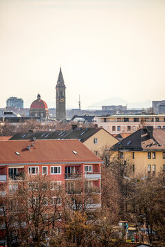 View of beautiful Pater Rupert Mayer Heim Kirche with its tower among rooftops and trees in an urban landscape, Munich, Germany.