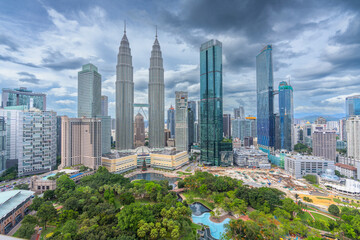 View of Petronas Towers and vibrant cityscape surrounded by greenery and cloudy sky, Kuala Lumpur, Malaysia.