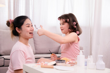 Asian mother and daughter share joyful bonding moment, explore makeup together, Take turns applying makeup,  young girl applies lipstick with mom while looking mirror,  learning, and warmth in home.