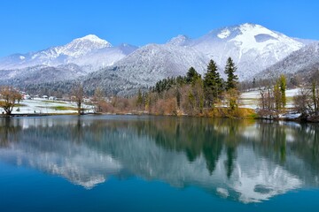 View of lake Črnava and Srednji vrh and Storžič mountains covered in snow above with a reflection of the mountains in the water in Gorenjska, Slovenia