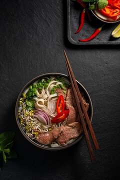 Top view of traditional Vietnamese beef pho noodle soup on dark background