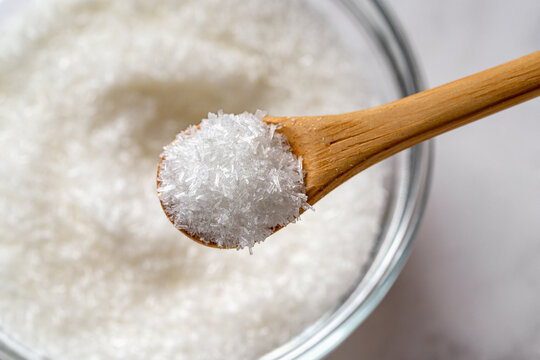Wooden spoon full of monosodium glutamate over MSG white crystals in a glass bowl macro close-up. Concept of flavor enhancer food additive E621.