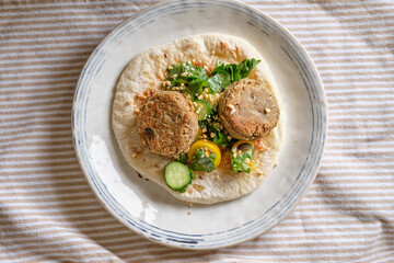 Flatbread with chickpea patty, cherry tomatoes, lettuce, cucumber, cilantro and sesame seeds
