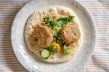 Flatbread with chickpea patty, cherry tomatoes, lettuce, cucumber, cilantro and sesame seeds