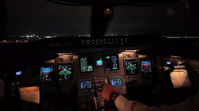 An immersive view inside a jet airplane of the cockpit during a night approach to the airport runway illuminated ahead. copilot is piloting. 4K