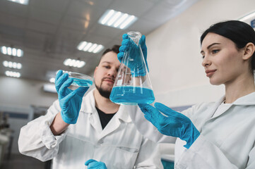Two scientists, man and woman, teamwork in research laboratory with chemical glassware, reagents,...