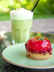 Small red dessert sits on a green plate next to a tall glass of green liquid