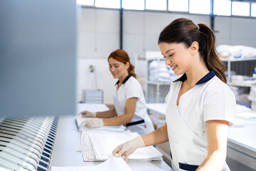 Female laundry workers folding linen and bedsheets after ironing in dry cleaning service.