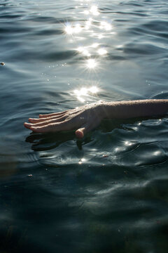 Hand touching water under sunlight with sparkling reflections