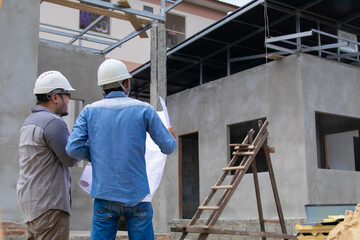 Fototapeta premium Two architect, foremen, contractor, builder male talking inspection on construction site, Indian engineering man and young project manager partner working together at workplace wearing safety helmet