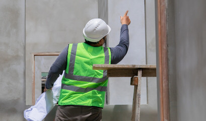 Asian overweight construction project foreman inspects construction site holding blueprint...