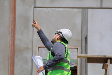 Asian overweight construction project foreman inspects construction site holding blueprint paperwork, engineering architect contractor man worker wearing safety helmet working in workplace outdoor