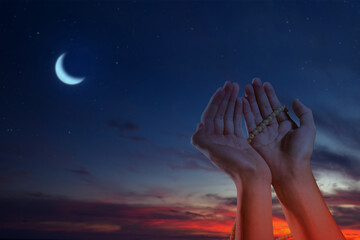 Muslim man praying with prayer beads and a crescent moon in the night scene background. Concept of...
