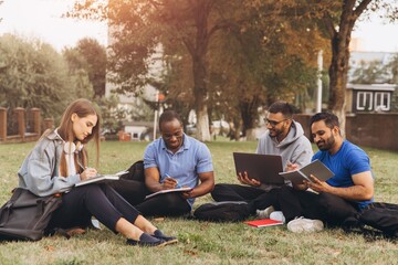 Group of Diverse College Students Studying Outdoors on Campus Lawn with Laptops and Notebooks