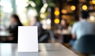 Obraz premium Close-up photo of a blank white table tent card on a modern cafe table, with people in the background out of focus. 