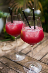 Red cocktail with ice in glass with stem on wooden surface