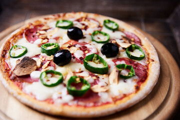 Pizza with salami and mozzarella cheese, jalapeno pepper and black olives. Wooden background. Soft focus. Close up.	