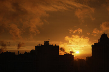 Obraz premium Colorful sunset over city buildings. Night city scene. Sunset view in the city, view from the roof. Silhouettes of buildings in the shadow, in the background the sun's rays painted the sky orange.
