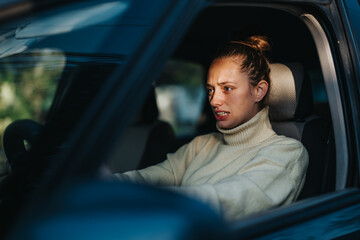Obraz premium A woman sits in the driver's seat, showcasing expressions of frustration and anxiety. The image captures a moment of stress during a drive, emphasizing strong emotions and intensity.