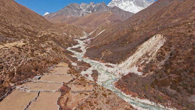 Snow capped Mount Everest towering over winding river, carving path through rocky Himalayan valley, displaying wilderness of Nepal in the Shomare to Dingboche Route