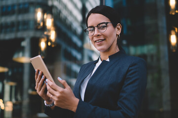Fototapeta premium Female office worker in formal wear smiling while using digital tablet at city street