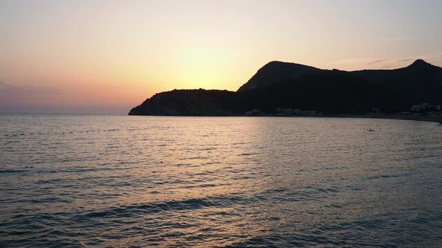 Waves gently lap at shore during stunning sunset over ocean. Sunlight reflects off waves as they roll onto shore, creating tranquil atmosphere at sunset by sea. Montenegro summer. Canj, Bar district