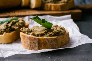 Healthy food, delicious and appetizing sandwiches with beef liver, parsley and aromatic baguette with crispy crust on sandwich paper close-up on dark background
