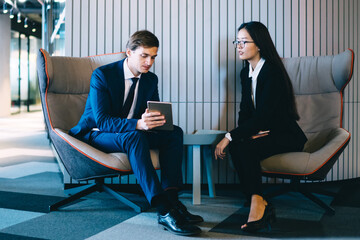 Multiethnic office employees in formal wear browsing gadgets at lobby of business center