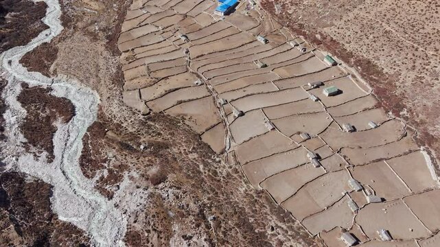 Aerial view revealing Himalayan Dingboche village, featuring traditional stone dwellings, steep agricultural terraces, mountainous landscape with distant peaks