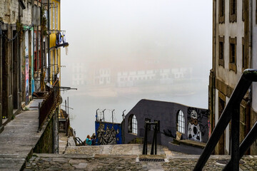 Fototapeta premium Stair street in old town Porto with vibrant color buildings and view on Douro river hdden in fog. Porto, Portugal.