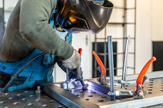 Welder joining metal parts using welding torch in workshop