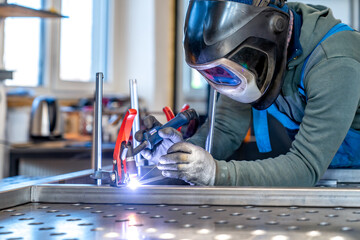 Metalworker welding metal frame in workshop wearing protective gear
