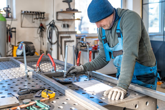 Welder using clamps and measuring tools on metal workbench