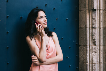 Fototapeta premium Dreamy woman speaking on smartphone outside old building