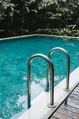 Swimming pool with clear blue water and metal handrails against a backdrop of tropical palm trees. Island Holiday Concept in a Hotel with Pool