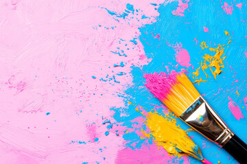 Obraz premium Paintbrush with Pink and Yellow Paint on a Textured Pink and Blue Background