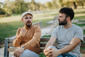 Two men engaged in a deep conversation while sitting on a park bench. The setting is outdoor,...